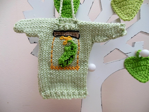 Hand knit green minature jumper ornament size 6 x 4.5 inches. A darker green pickled gherkin in a jar is the design on the front. There is a crochet attachment on the neck of the sweater for you to hang it up. A nitcraft label is placed on the bottom.