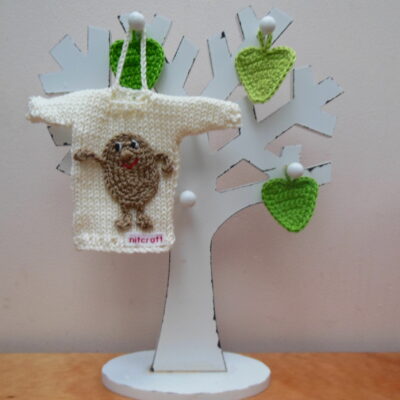 Hand knit minature jumper in cream with a brown positive potato applique hanging on a wooden tree photo prop.